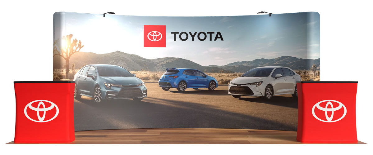 Trade show backdrop with Toyota logo and three Toyota cars on a desert road, flanked by red display podiums.