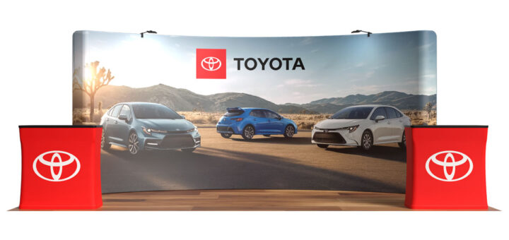 Trade show backdrop with Toyota logo and three Toyota cars on a desert road, flanked by red display podiums.